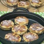 vegan Welsh cakes on a cast iron griddle with green stripy white tea towel underneath, in distance wire rack with cooked cakes and small brown sugar dish/featured image.