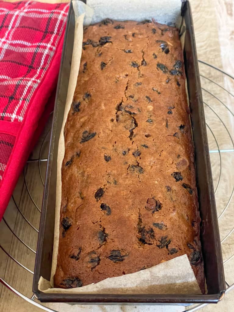 traditional fruit cake baked and still in baking pan on a wire rack, with red tartan oven mitt to side.