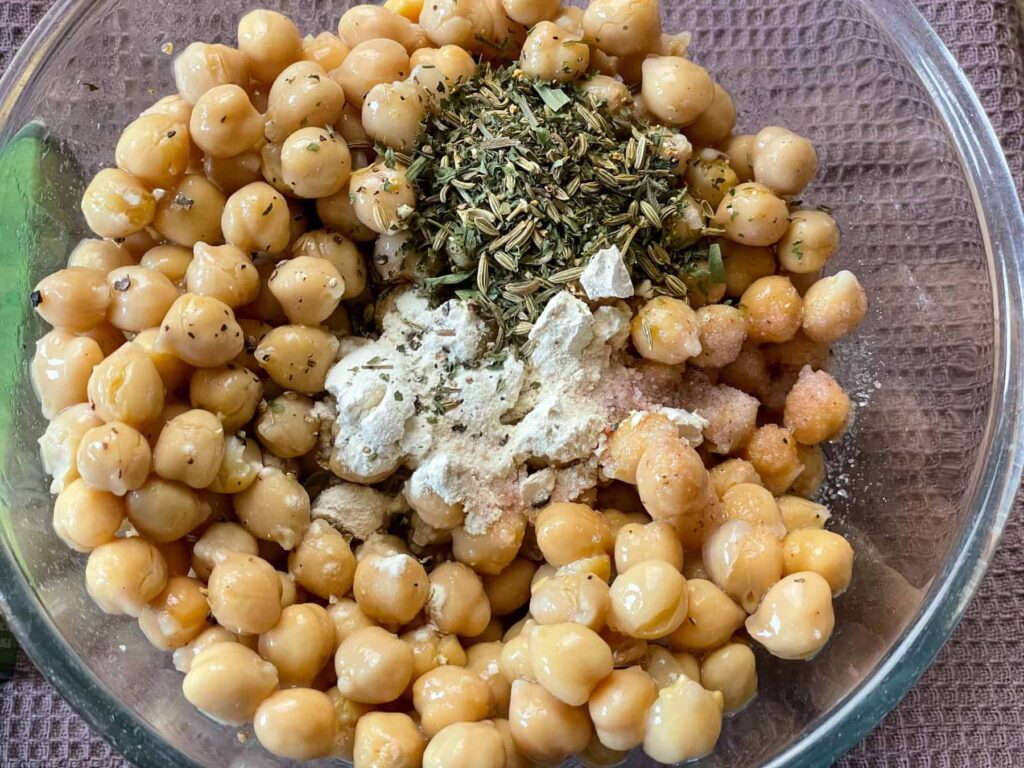 chickpeas in glass bowl with spices and herbs on top.