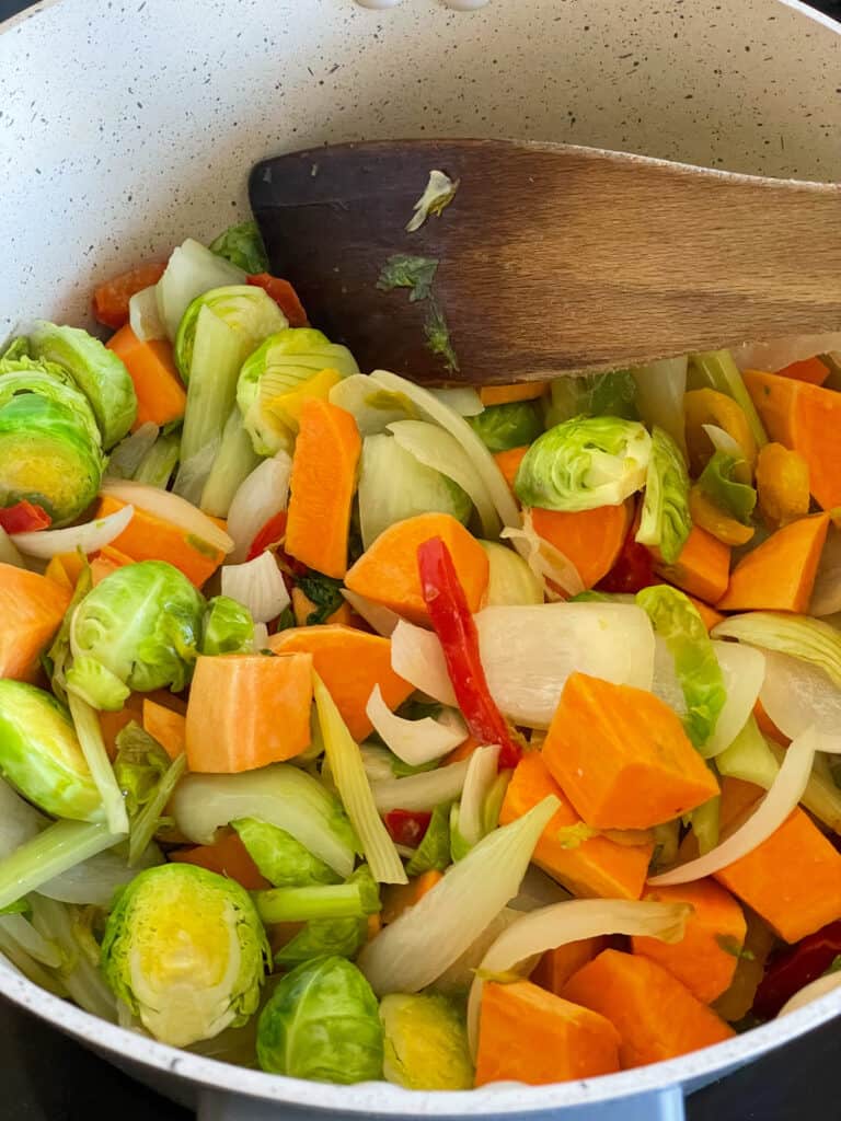 sweet potato chunks, mixed bell pepper slices and sliced Brussel sprouts added to onions in pot with wooden spatula stirring.