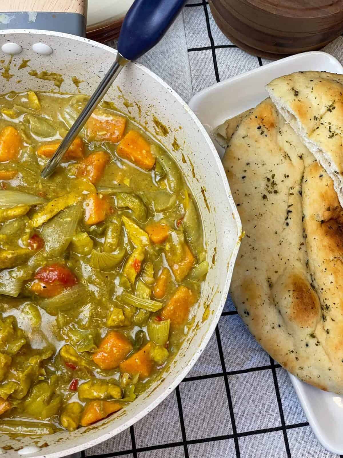 A bowl of curry with vegetables and bread on a table