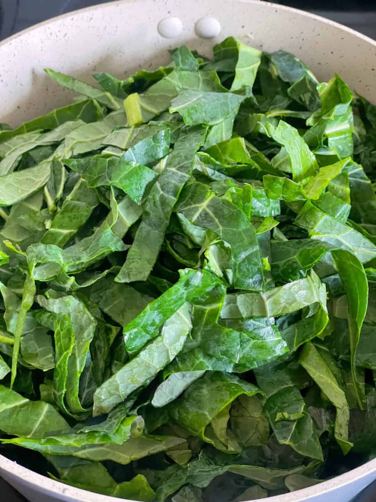 Shredded spring greens added to sauteing carrots and celery in pot.