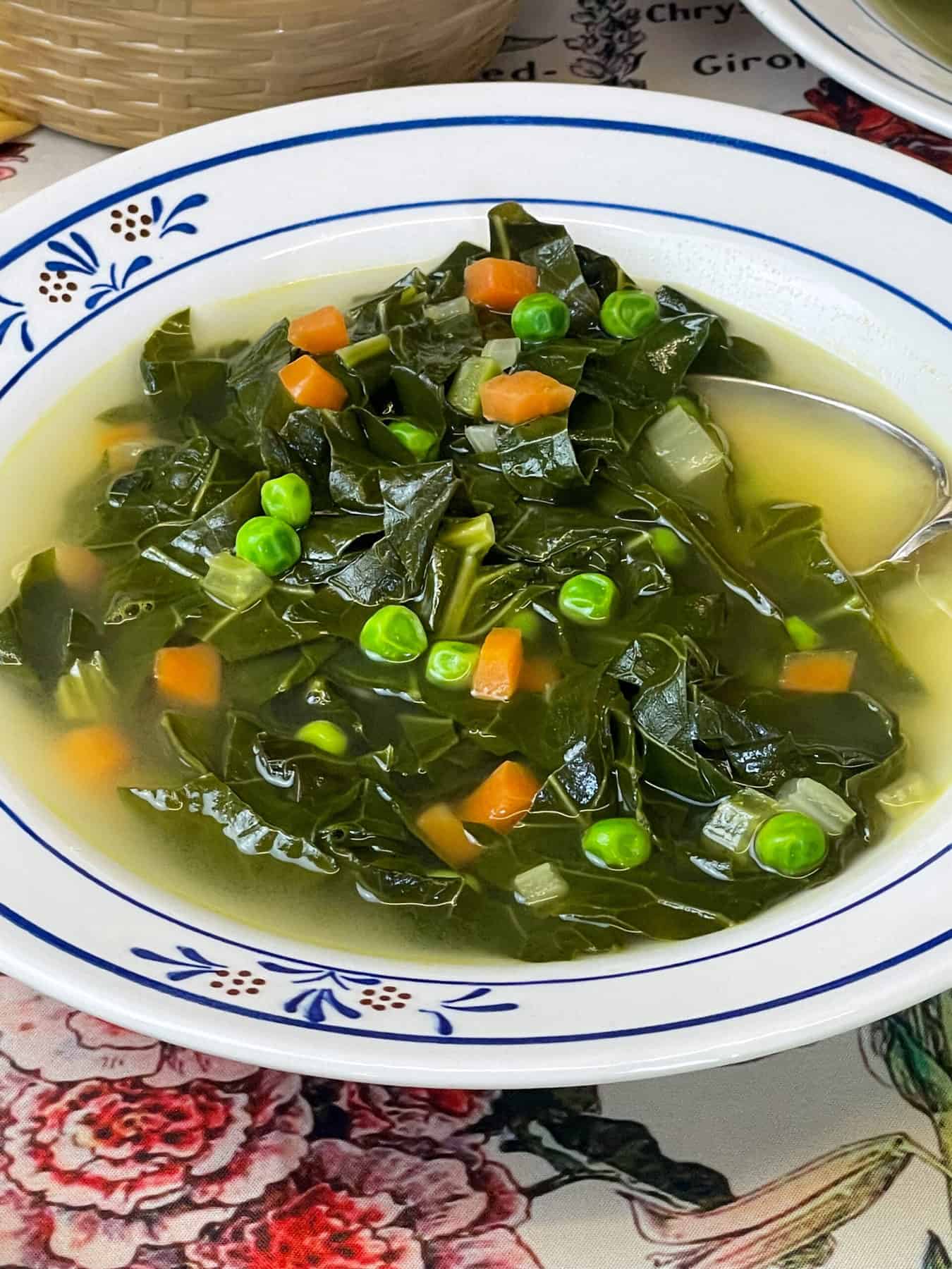 Close up soup with spoon in bowl and flower patterned bowl and table cloth.