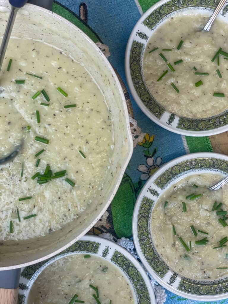 soup to side with potato soup and ladle, three small bowls with green pattern around rim to side and blue and green table cloth background.