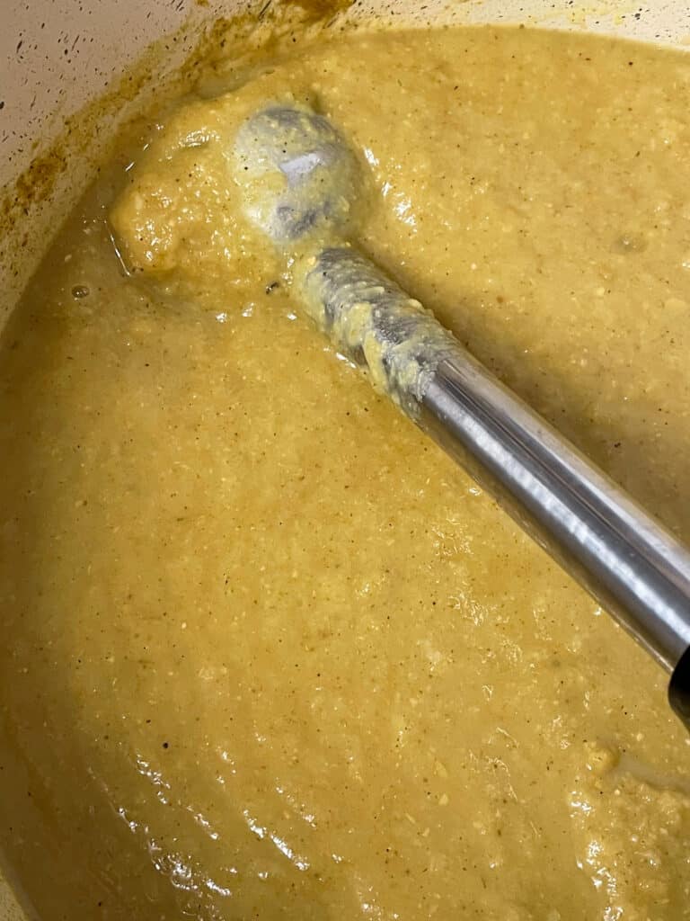 an immersion blender blending the soup until a smooth puree in the saucepan.