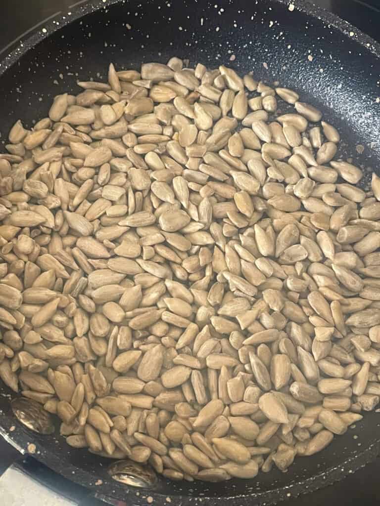 sunflower seeds added to small pan and toasting over a cooker ring.