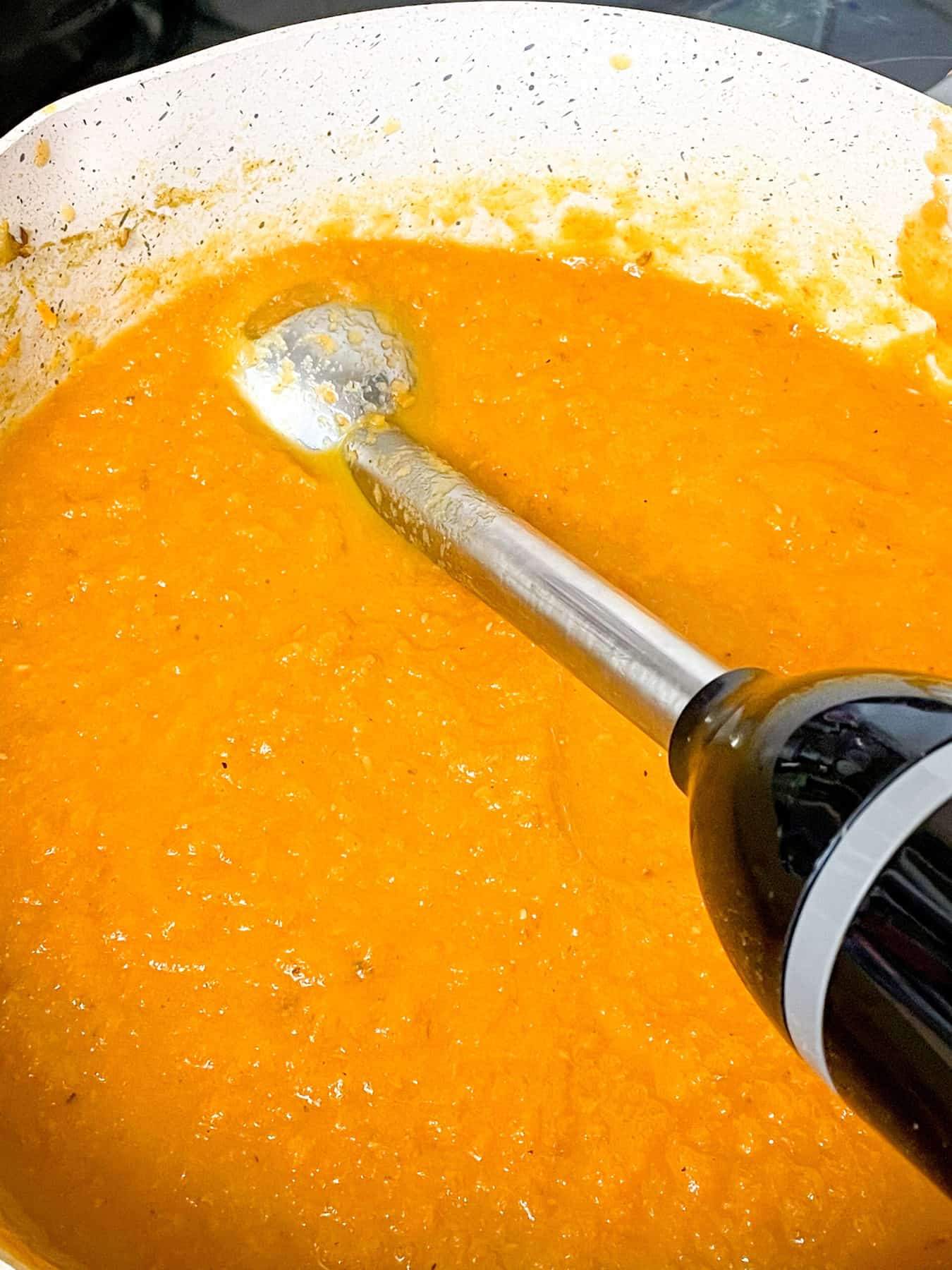 An immersion stick blender in the soup pot blending the soup to a puree.