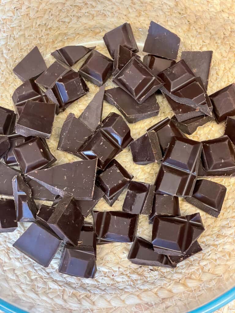 pieces of chocolate in glass bowl ready to be microwaved and melted, tan coloured mat underneath.