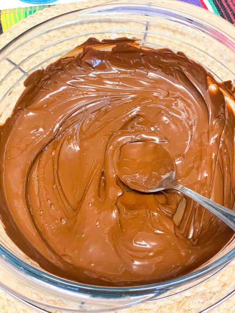 dark chocolate melted in glass bowl with silver spoon stirring.