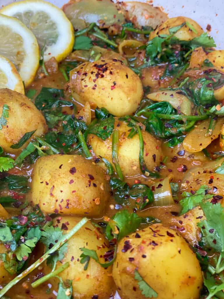 close up of Saag Aloo with lemon slices, cilantro and red chilli flake garnish.