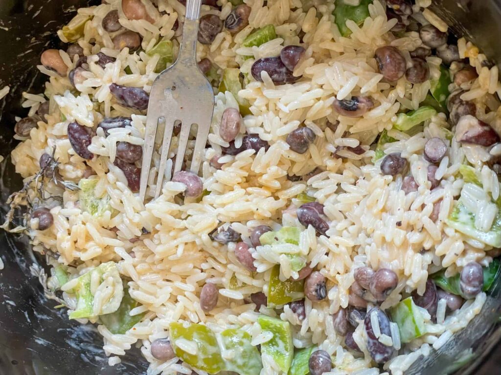 rice and peas being stirred and fluffed up with a silver fork within the slow cooker.