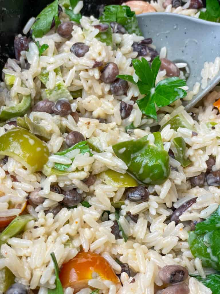 rice and peas garnished with fresh herbs being stirred with grey ladle, ready to serve.