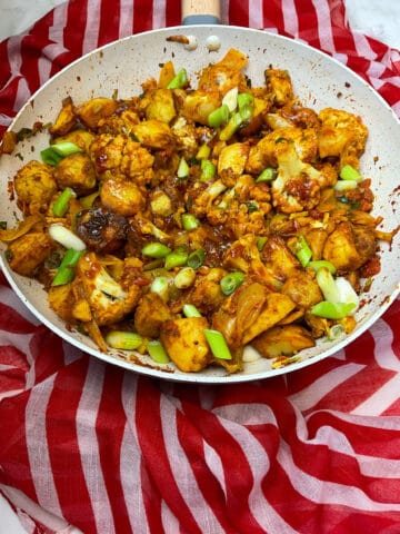 Aloo Gobi cooked and ready to serve in a large Wok, red and white stripy background.