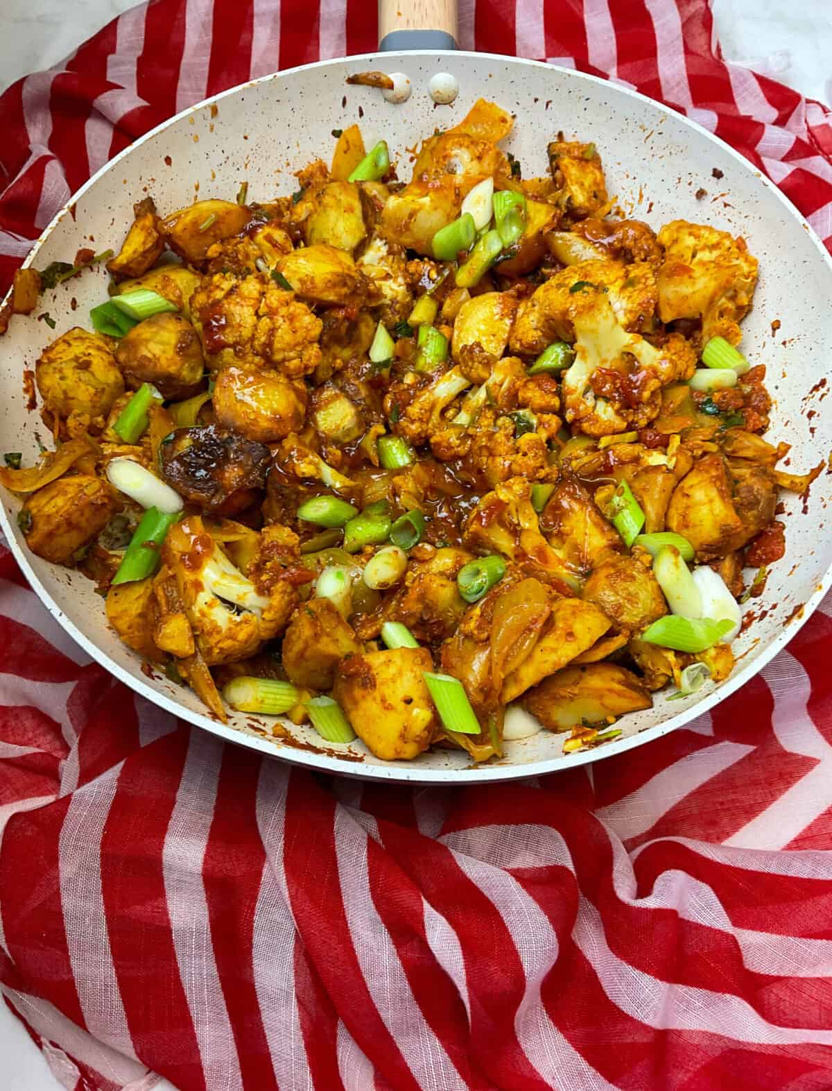 Aloo Gobi cooked and ready to serve in a large Wok, red and white stripy background.