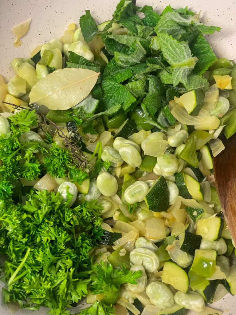 fresh herbs added to cooked veggies in pan.