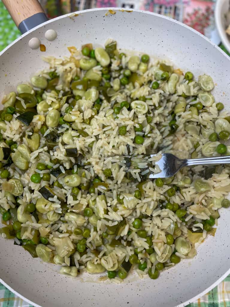 pea pilaf in pan with a silver fork fluffing up the grains.
