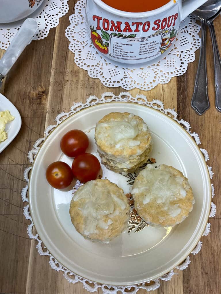scones served with cherry tomatoes, cup of tomato soup to background, white doily placemats, wooden background.