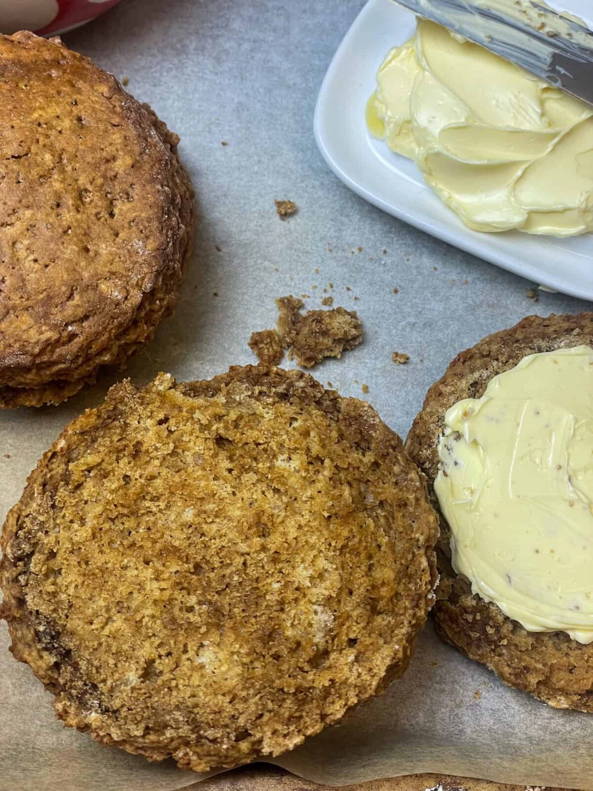 Treacle scones halved and one side buttered, second scone to side, and small butter dish to side with butter knife.