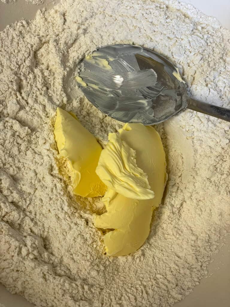 margarine added to dry ingredients with a silver spoon.