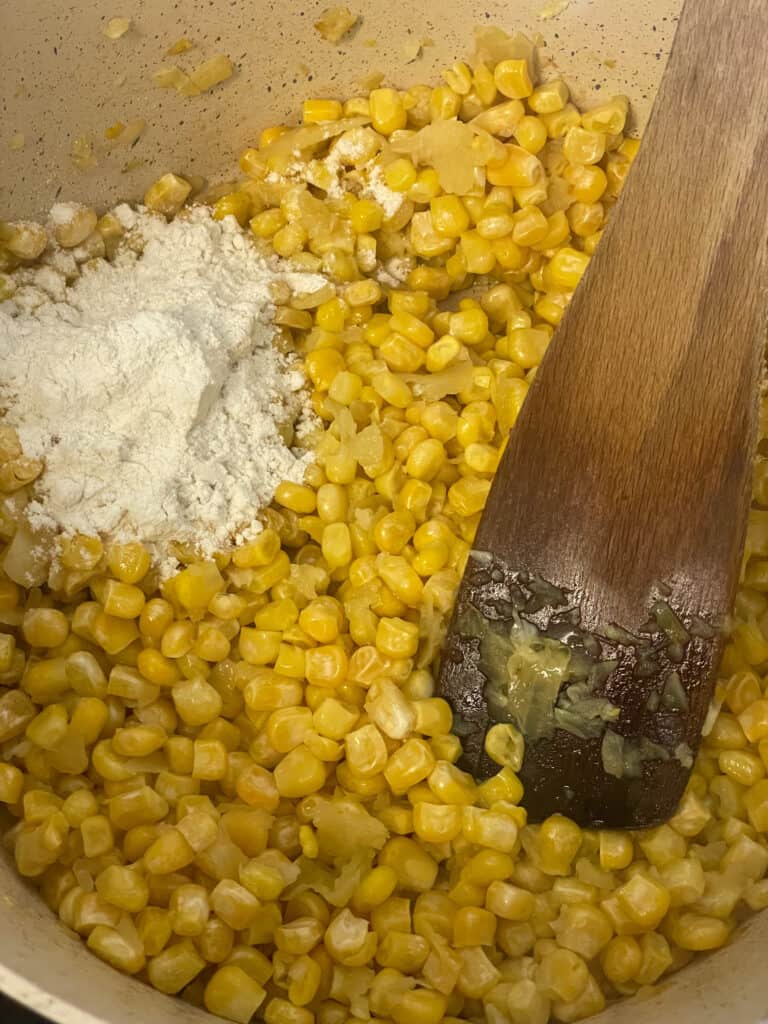 flour added to corn and onions cooking in saucepan with wooden spatula stirring.