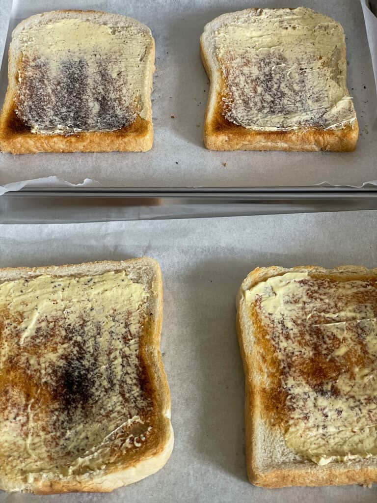 four slices of toasted bread spread with vegan margarine on baking tray.
