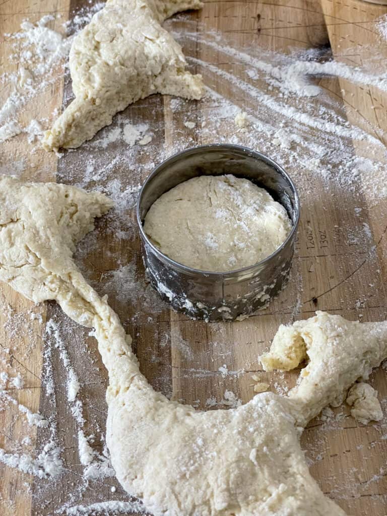 buttermilk scones stamped out with biscuit cutter on floured chopping board, scraps of dough to side.