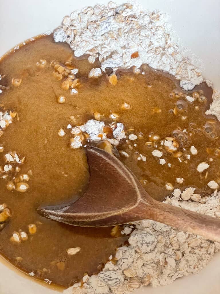 Wet ingredients poured into dry ingredients in mixing bowl with wooden spoon.