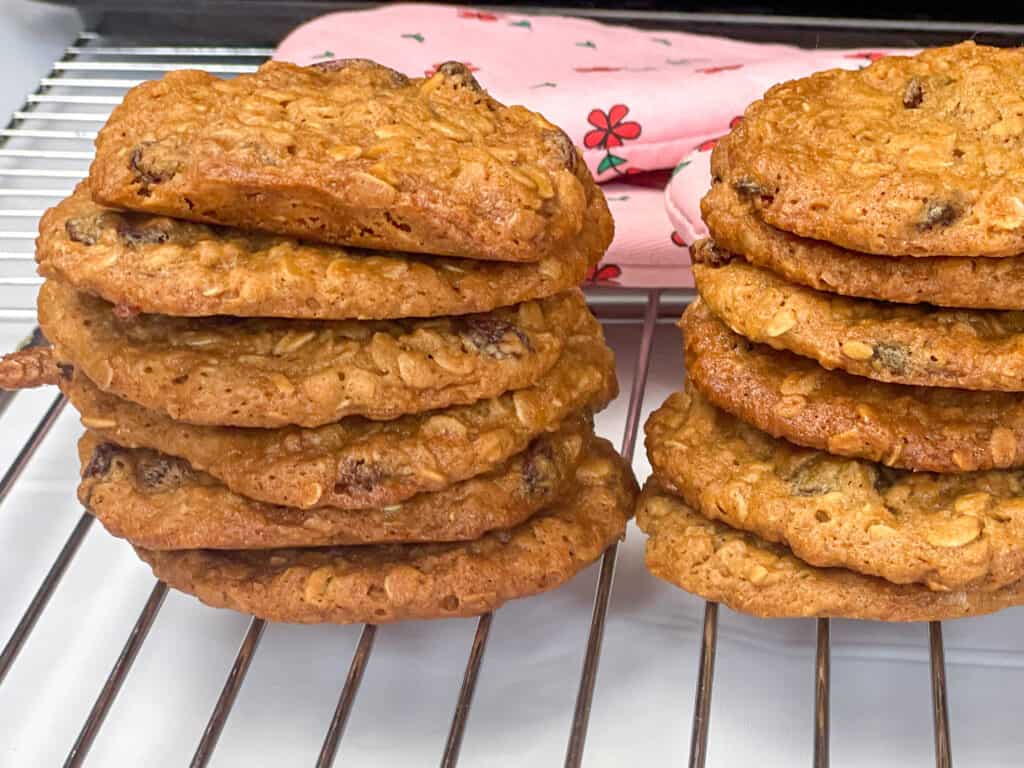 Oatmeal raisin cookies on wire rack cooling with pink flower oven mitts in background.