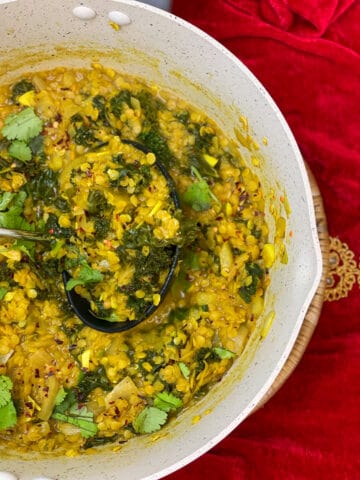 Red lentil and kale dahl cooked in pan and ready to serve, red velvet background.