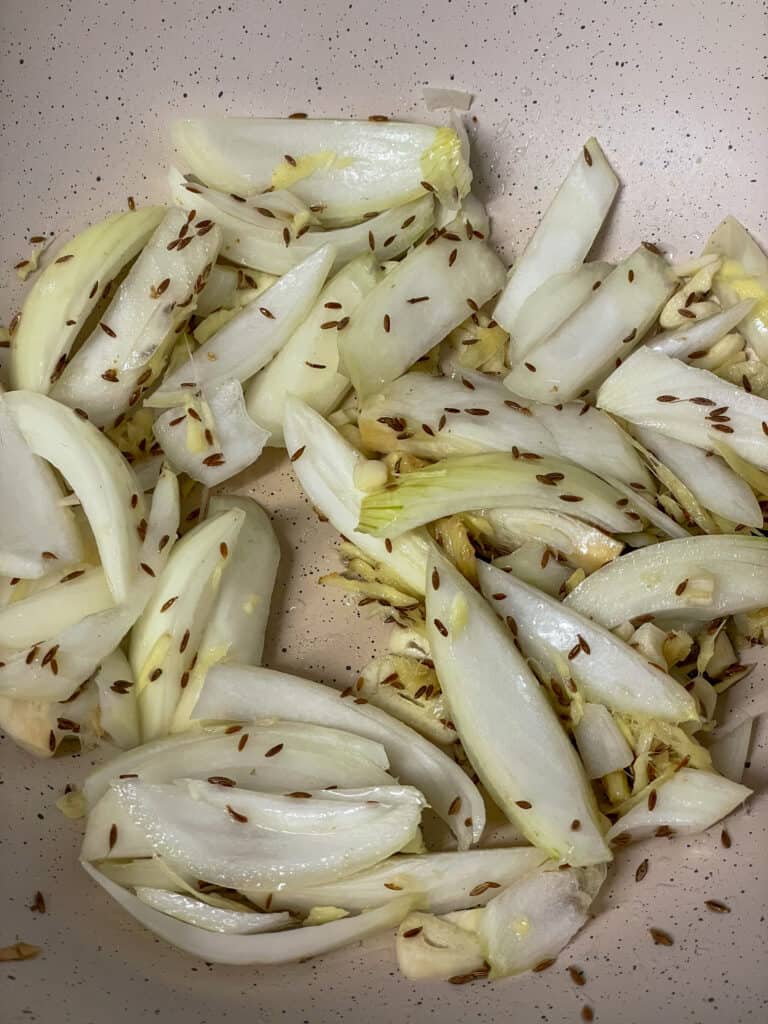 onions, garlic, ginger and cumin seeds cooking in cream coloured pan.