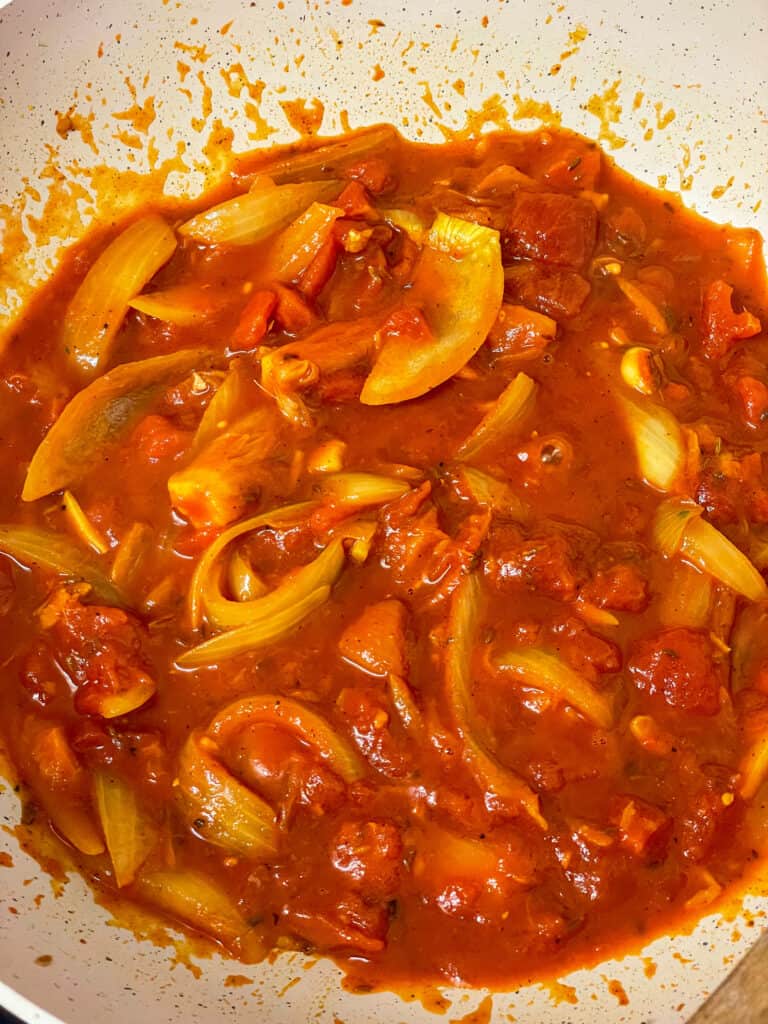 tomato paste and chopped tomatoes added to onions and spices in the pan.