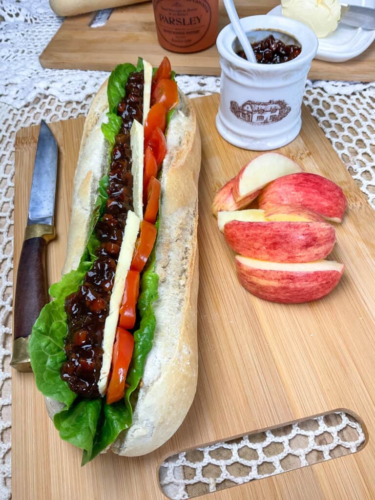 Apple slices at the side of filled baguette on cutting board.