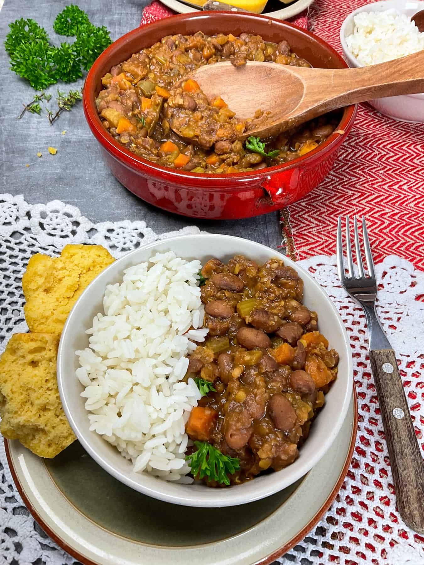 A bowl of beans and rice, with cornbread muffins to side, bowl of rice to side, crochet table cloth.