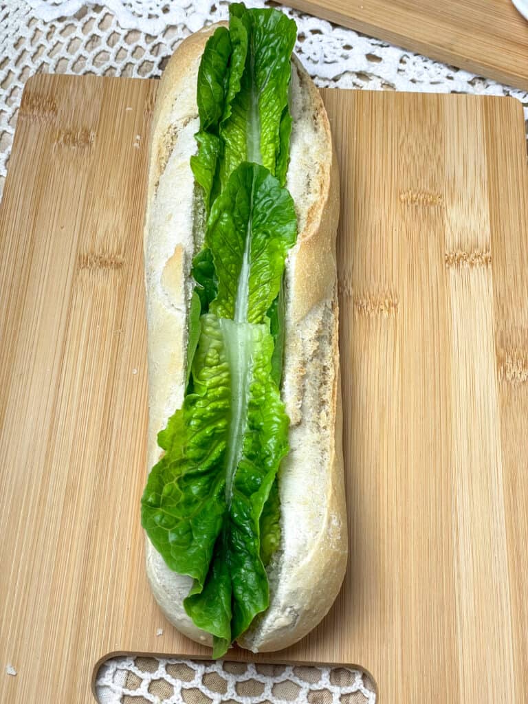 Lettuce added to baguette on cutting board.