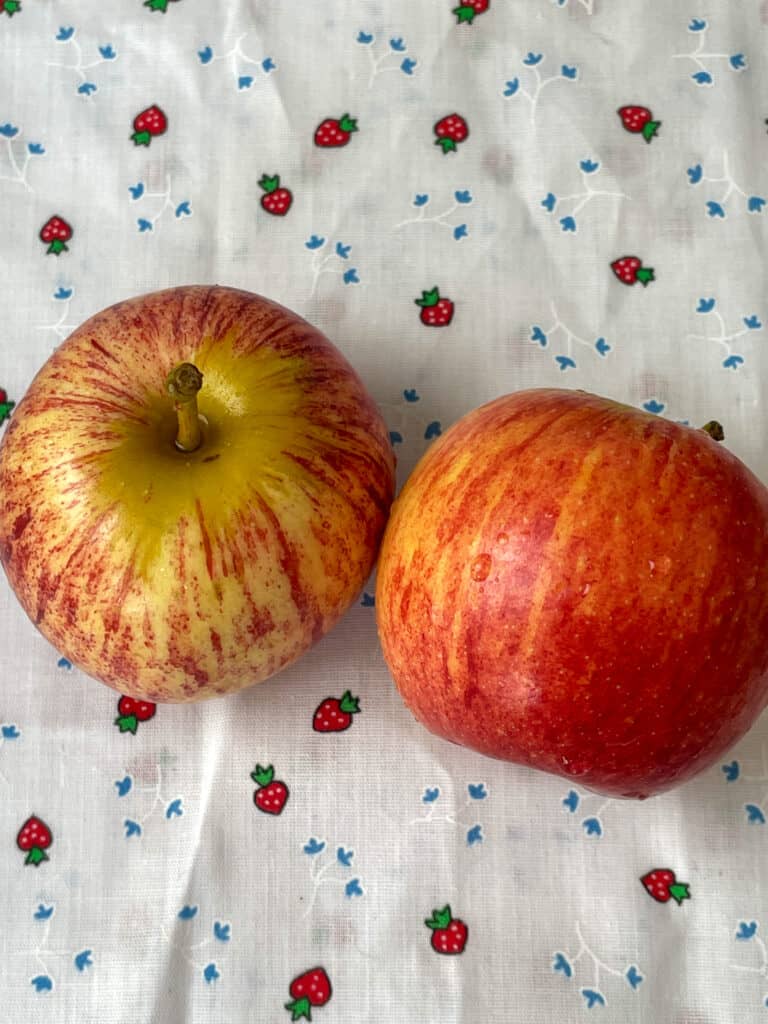 Two red apples on a white tablecloth with little strawberry pattern.