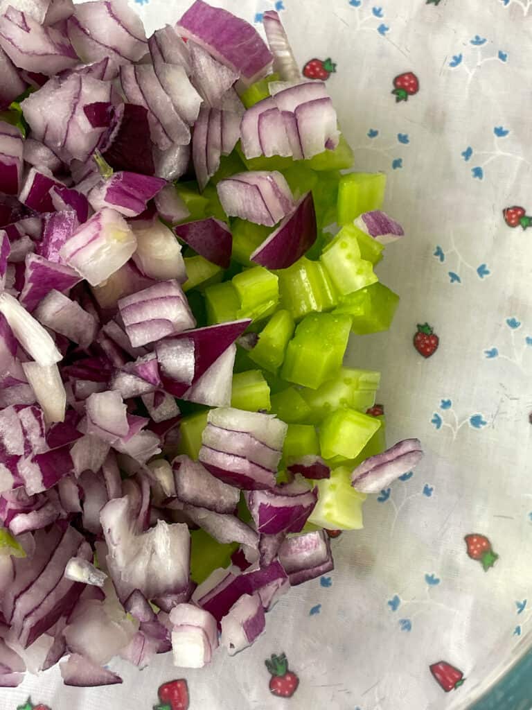 Diced red onion and celery in glass bowl.