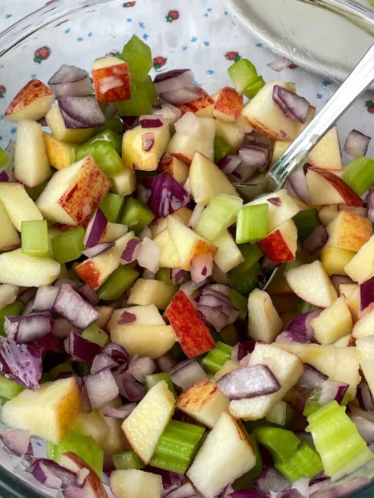 Diced fruit and veggies for Waldorf salad in glass bowl with silver spoon.