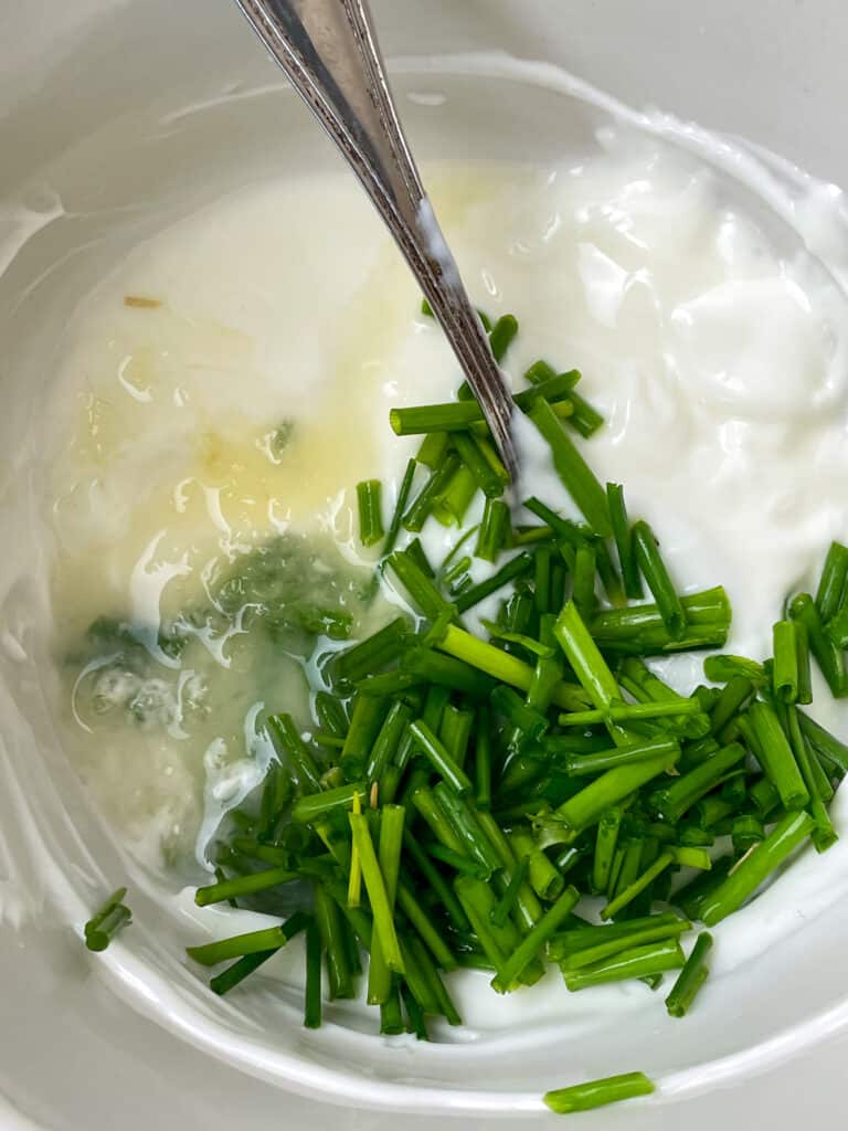 Salad dressing ingredients and chives in bowl with spoon to mix.