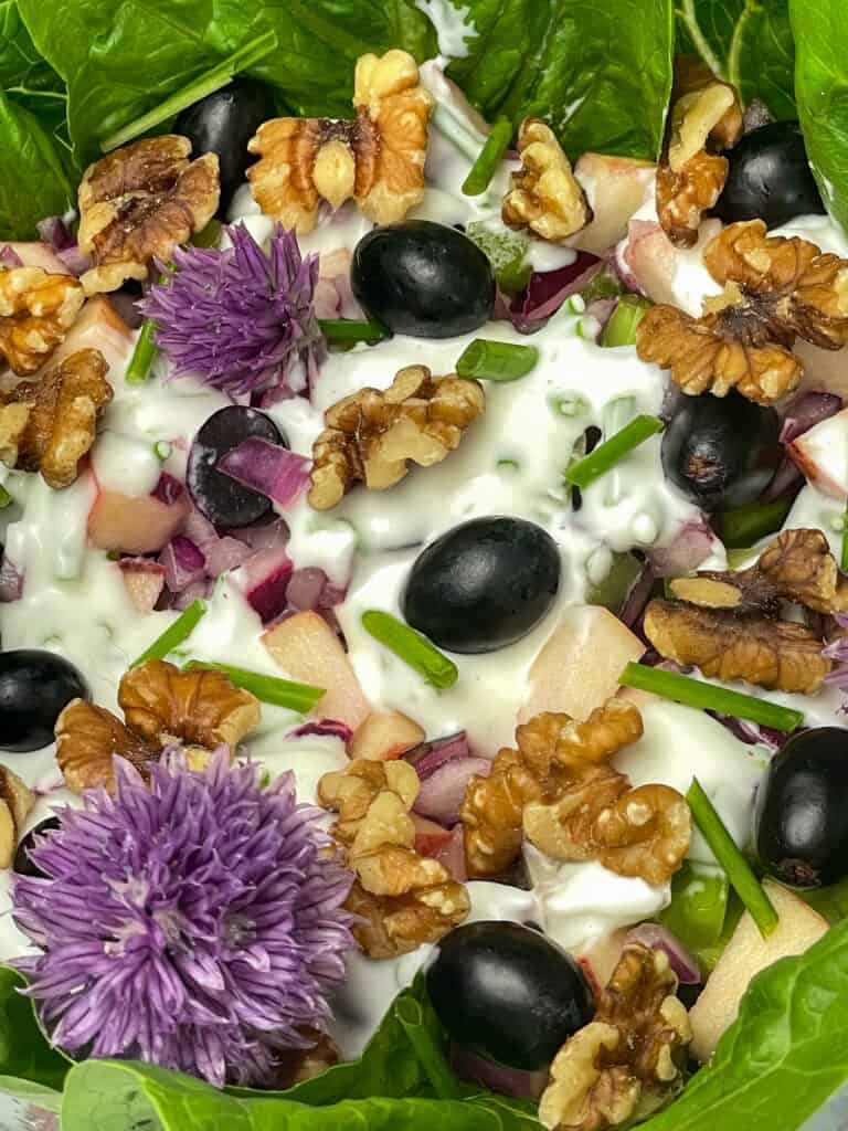 Close up of vegan Waldorf salad garnished with chive flowers, walnuts and grapes.