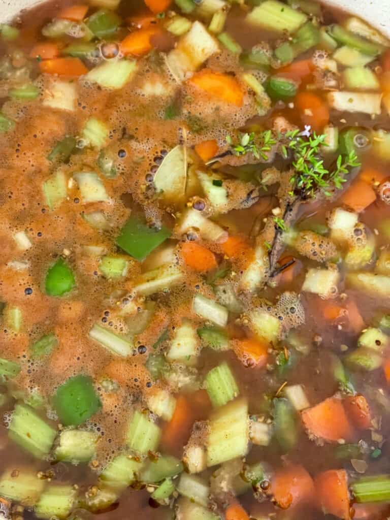 veggie stock added to red beans stew ingredients within saucepan.