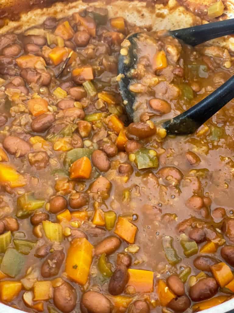 potato masher mashing some of the stew in the saucepan.