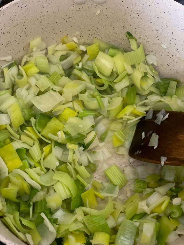 leeks sauteing in soup pot with wooden spatula.