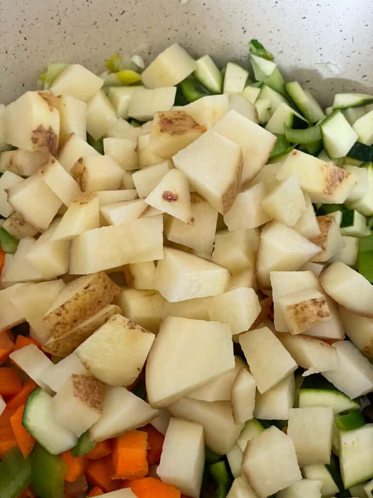 chopped potatoes added to veggies in soup pot.