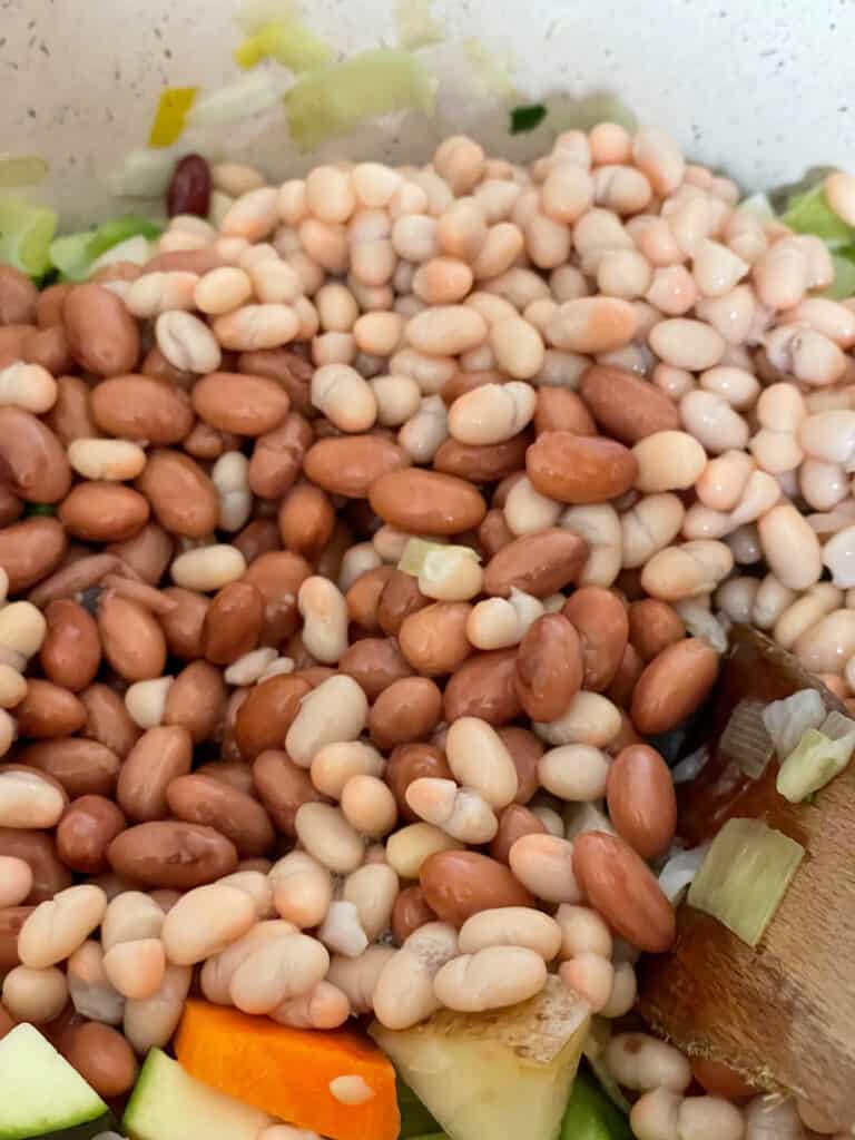 pinto and cannellini beans added to veggies in soup pot.