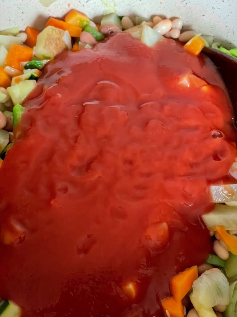 tomato passata added to beans and veggies in soup pot.