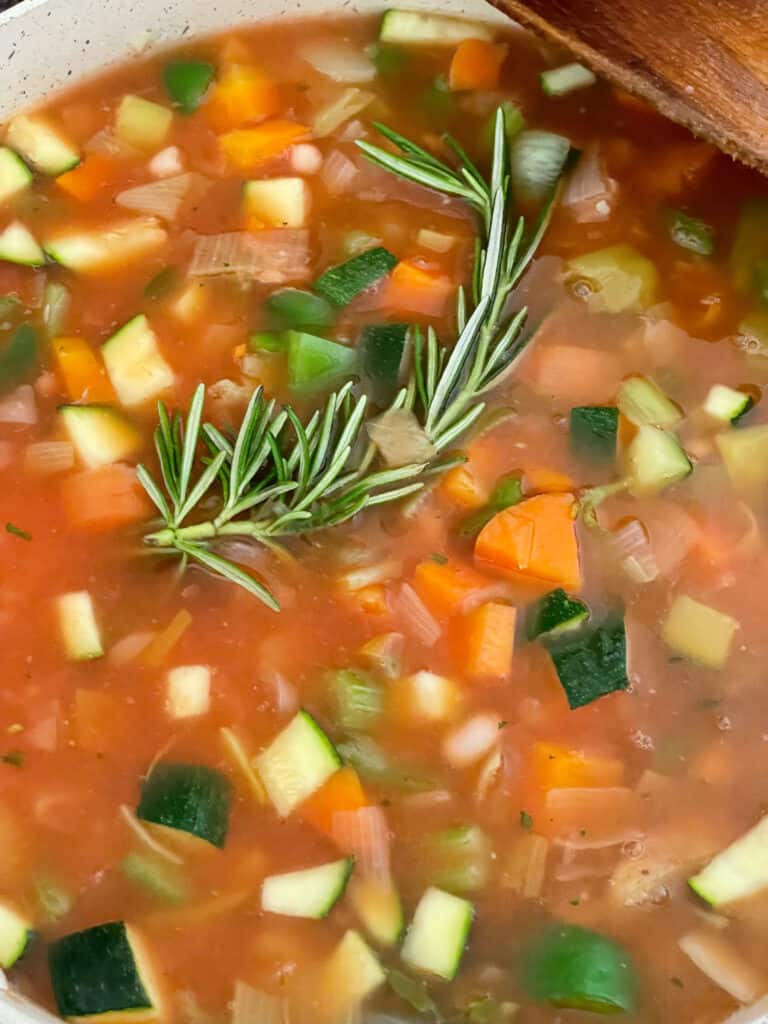 cabbage and bean soup stirred and sprig of rosemary added to soup pot.