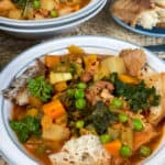 A close up bowl of Italian cabbage and bean soup with second bowl in background and plate of crusty bread to side.