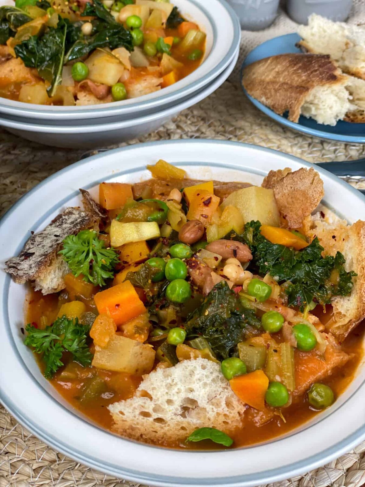 A close up bowl of Italian cabbage and bean soup with second bowl in background and plate of crusty bread to side.