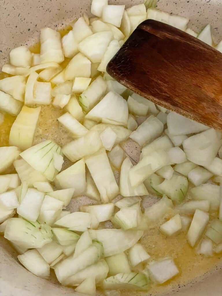 Onions cooking in melted margarine in soup pot with wooden spatula.