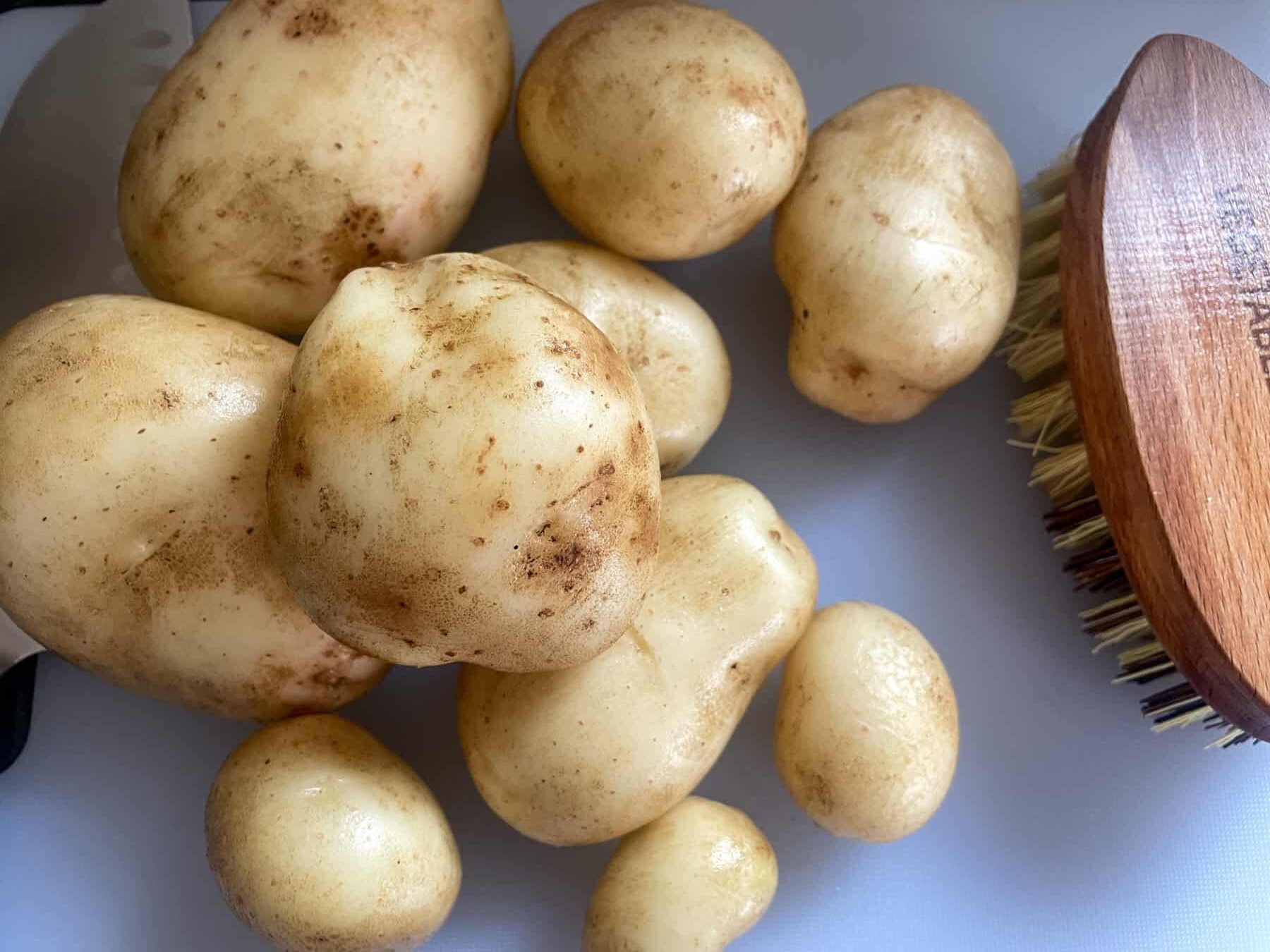 Carlingford potatoes on white chopping board with vegetable brush to side.